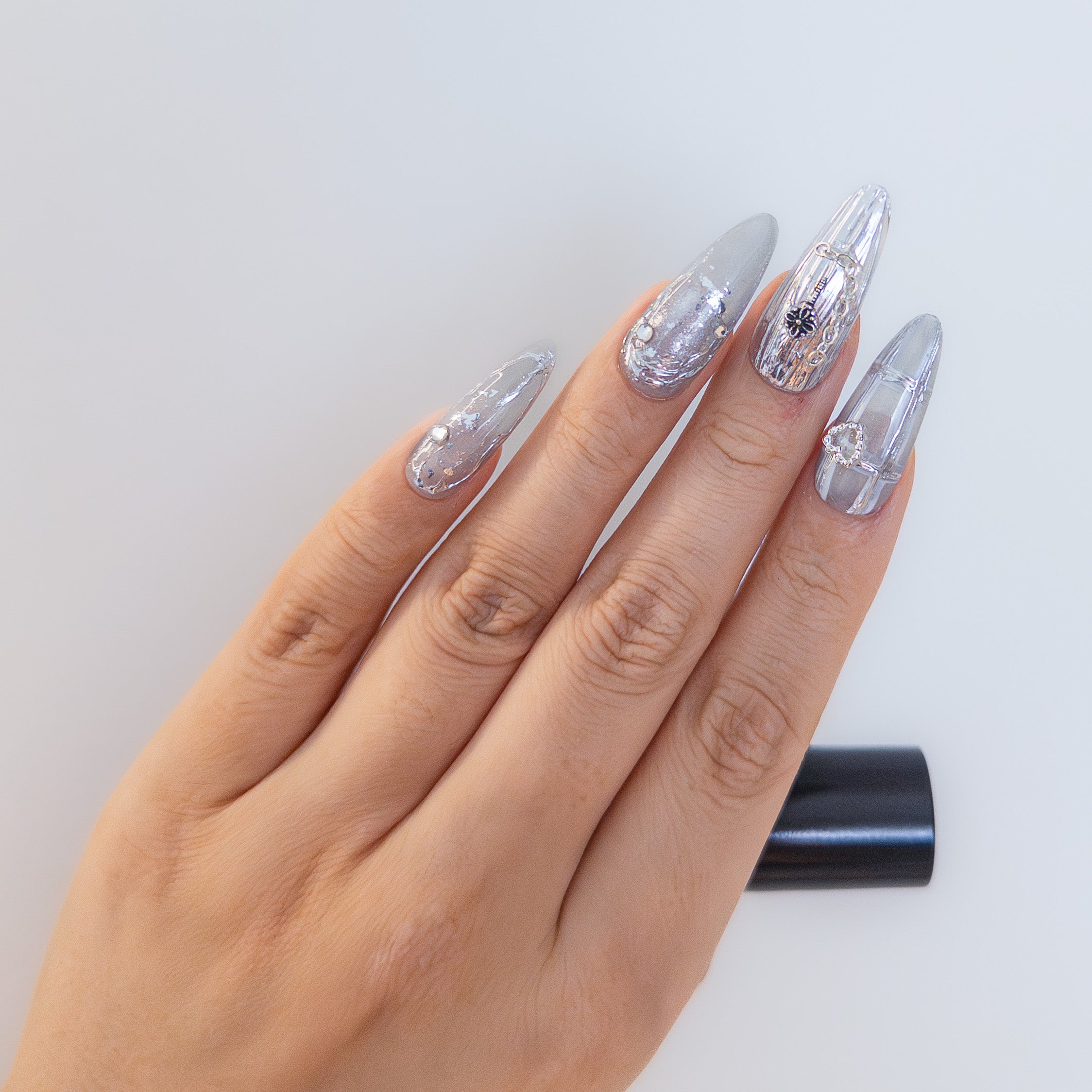 Macro detail of 3D silver chain hardware, cross charm, and textured metallic swirls on high-gloss chrome structured gel nails.