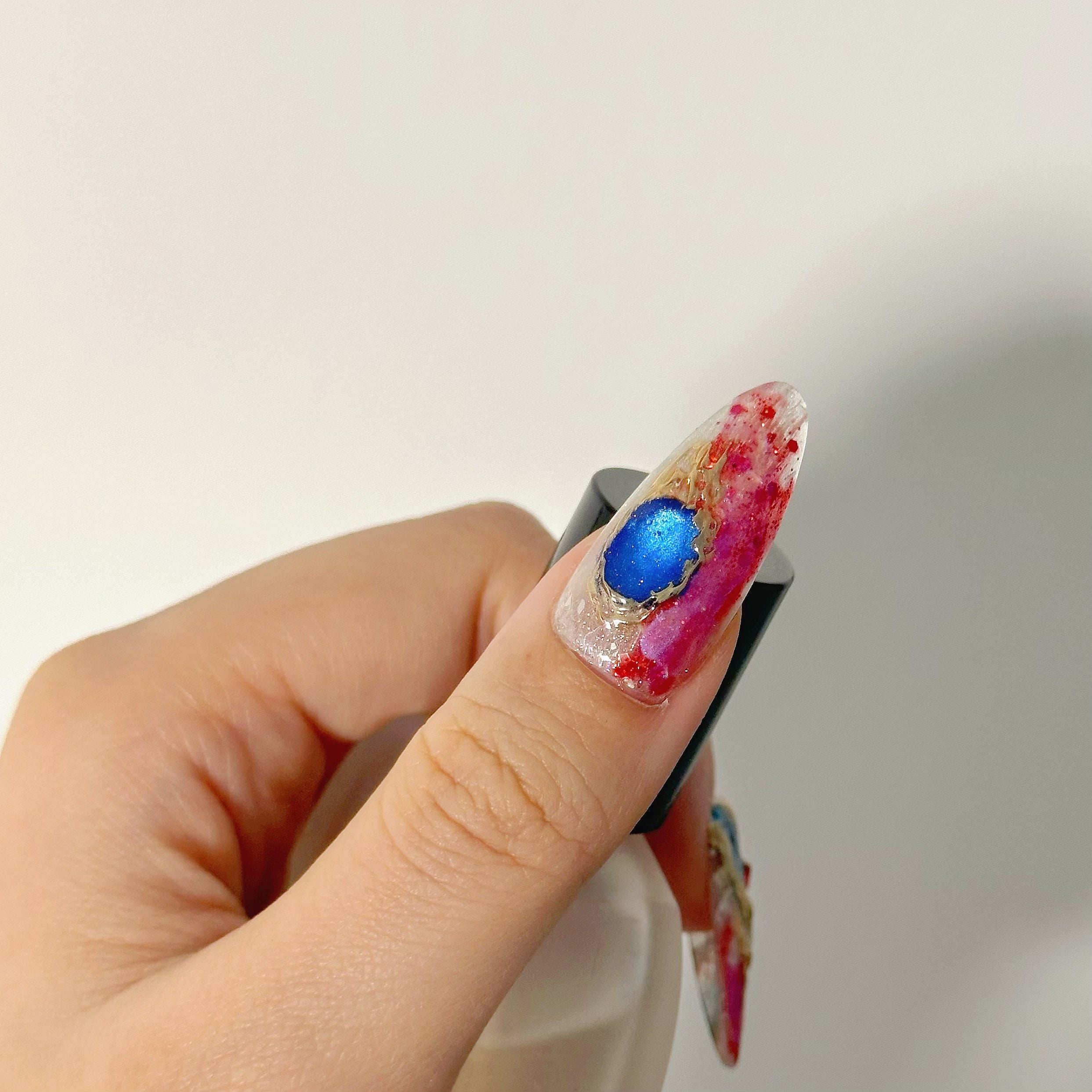 Large blue gemstone encrusted in gold chrome on abstract red marble luxury reusable gel.