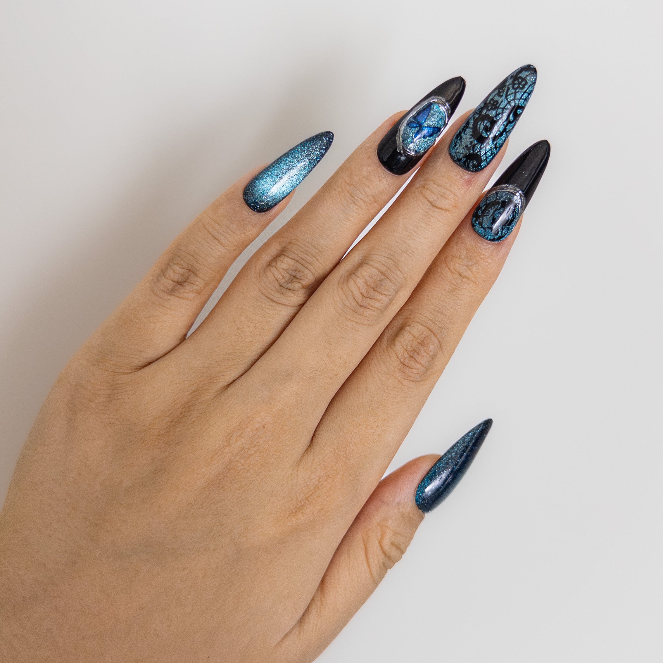 Magnetic blue cat-eye gel featuring intricate hand-painted black lace and 3D butterfly gem on salon-grade structured nails.