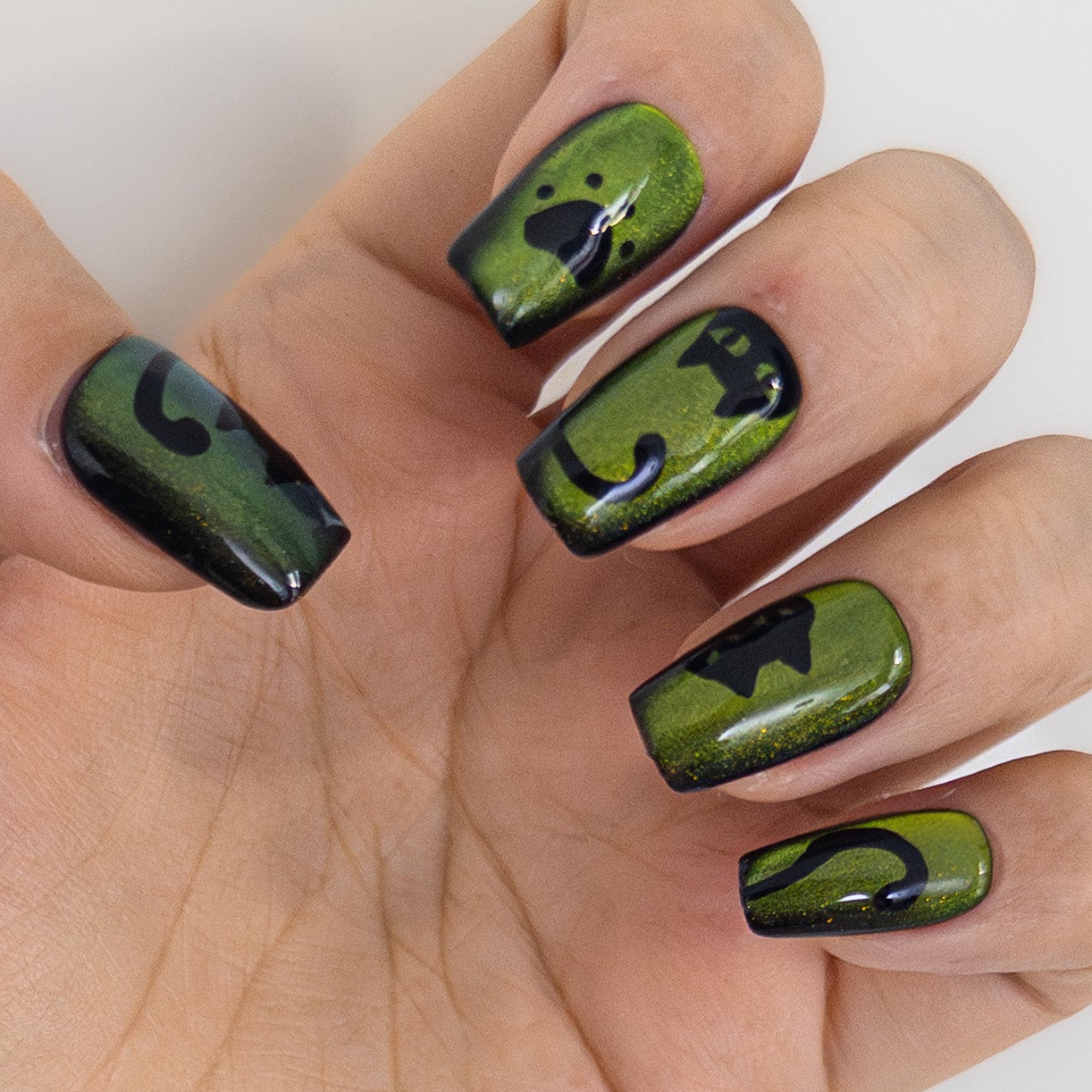 Side view of shimmering green magnetic gel with hand-painted black cat silhouettes on salon-grade structured square nails.