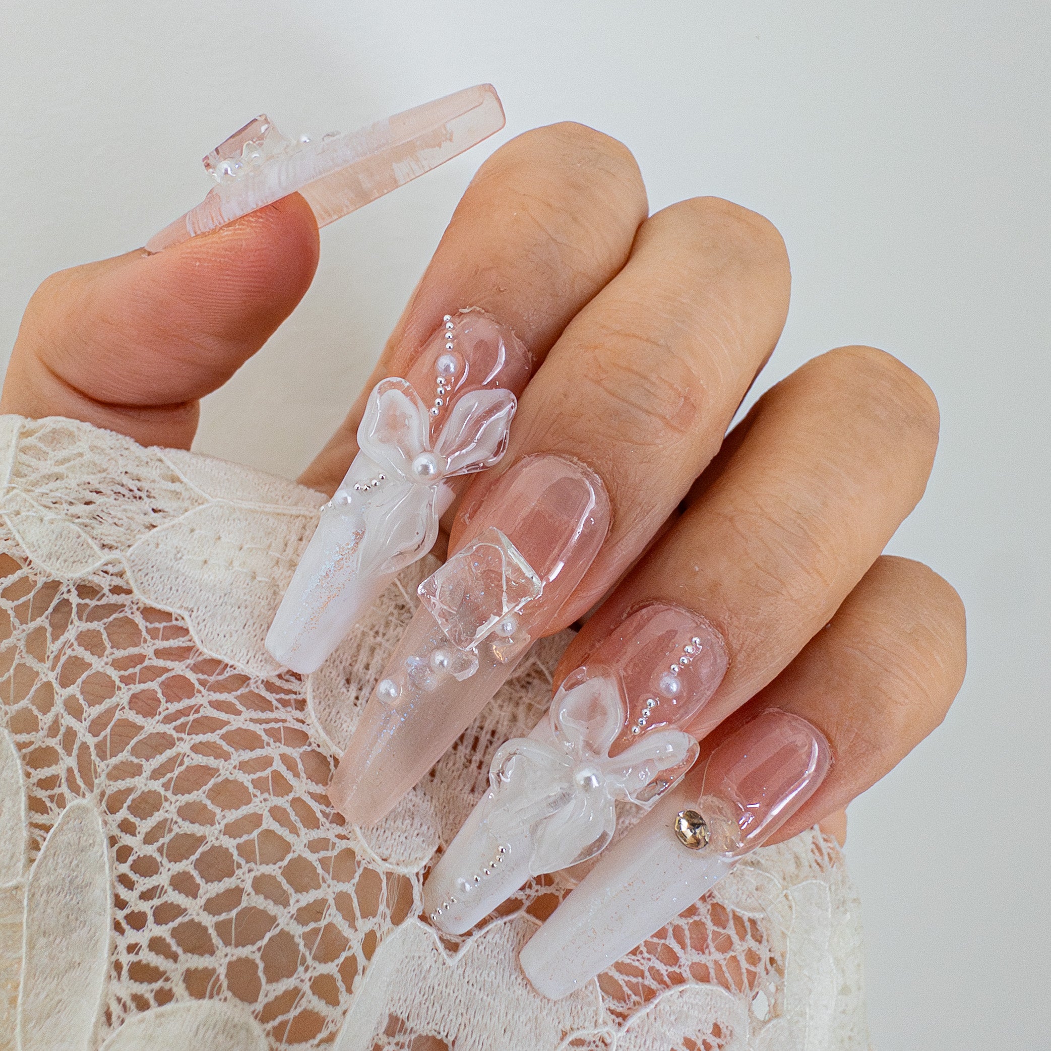 Close-up of Pearl Veil handcrafted press-on nails featuring 3D sculpted white bows and pearl accents on a lace background.