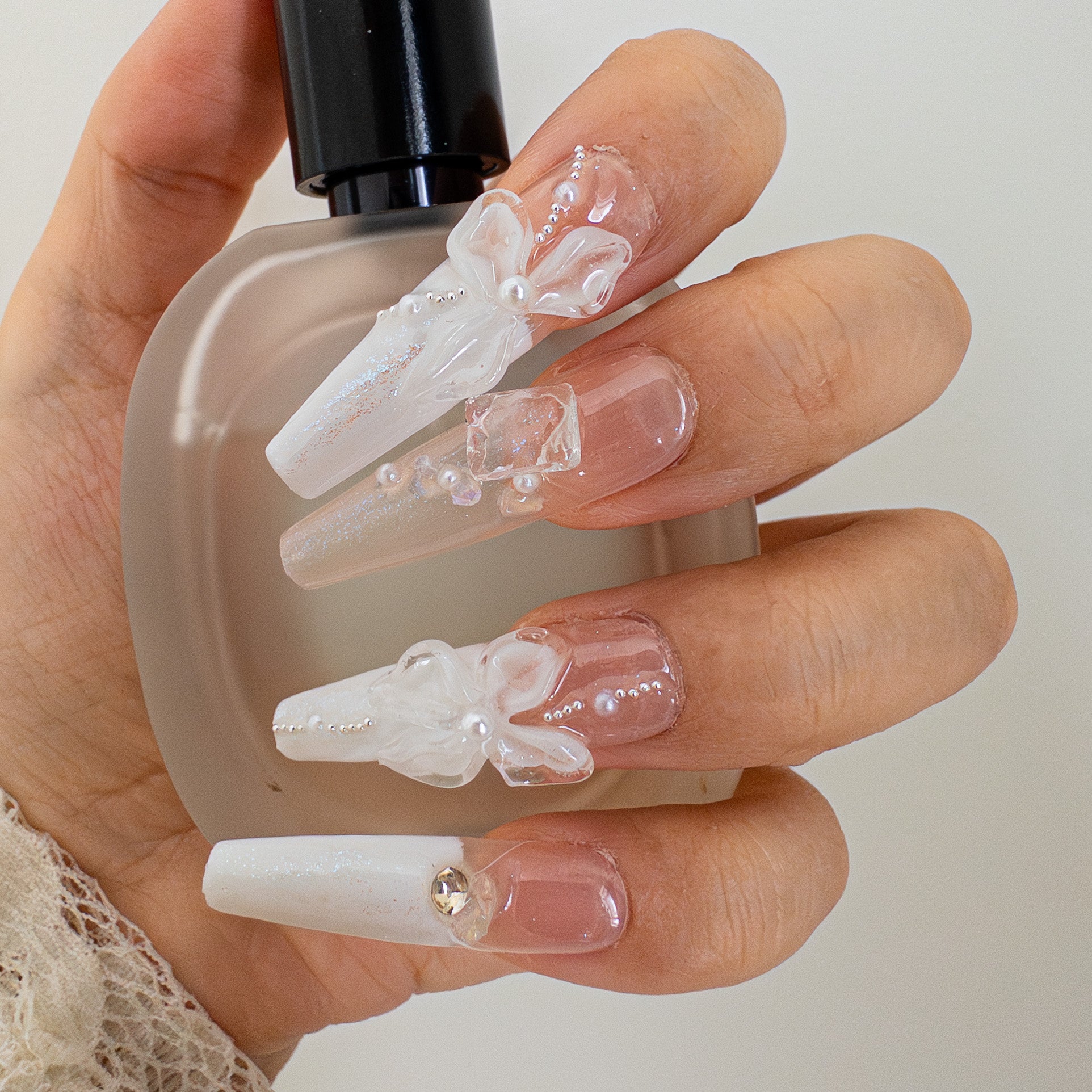 Pearl Veil reusable press-on nails held against a frosted glass bottle, highlighting the elegant white and clear design with hand-sculpted textures.