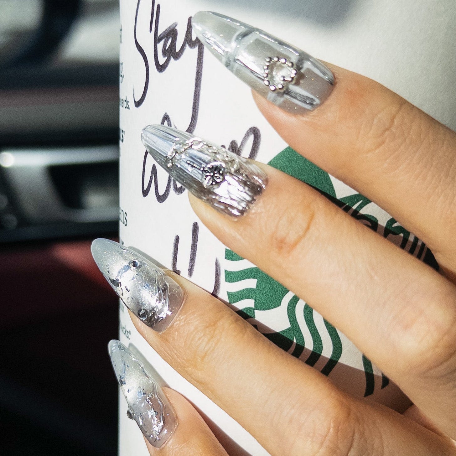 Long stiletto press on nails featuring an edgy silver chrome design. The set blends textured metallic finishes with distressed translucent foil accents. Decorated with 3D silver charms including a crystal heart, cross, and delicate chains for a Y2K cyberpunk aesthetic.