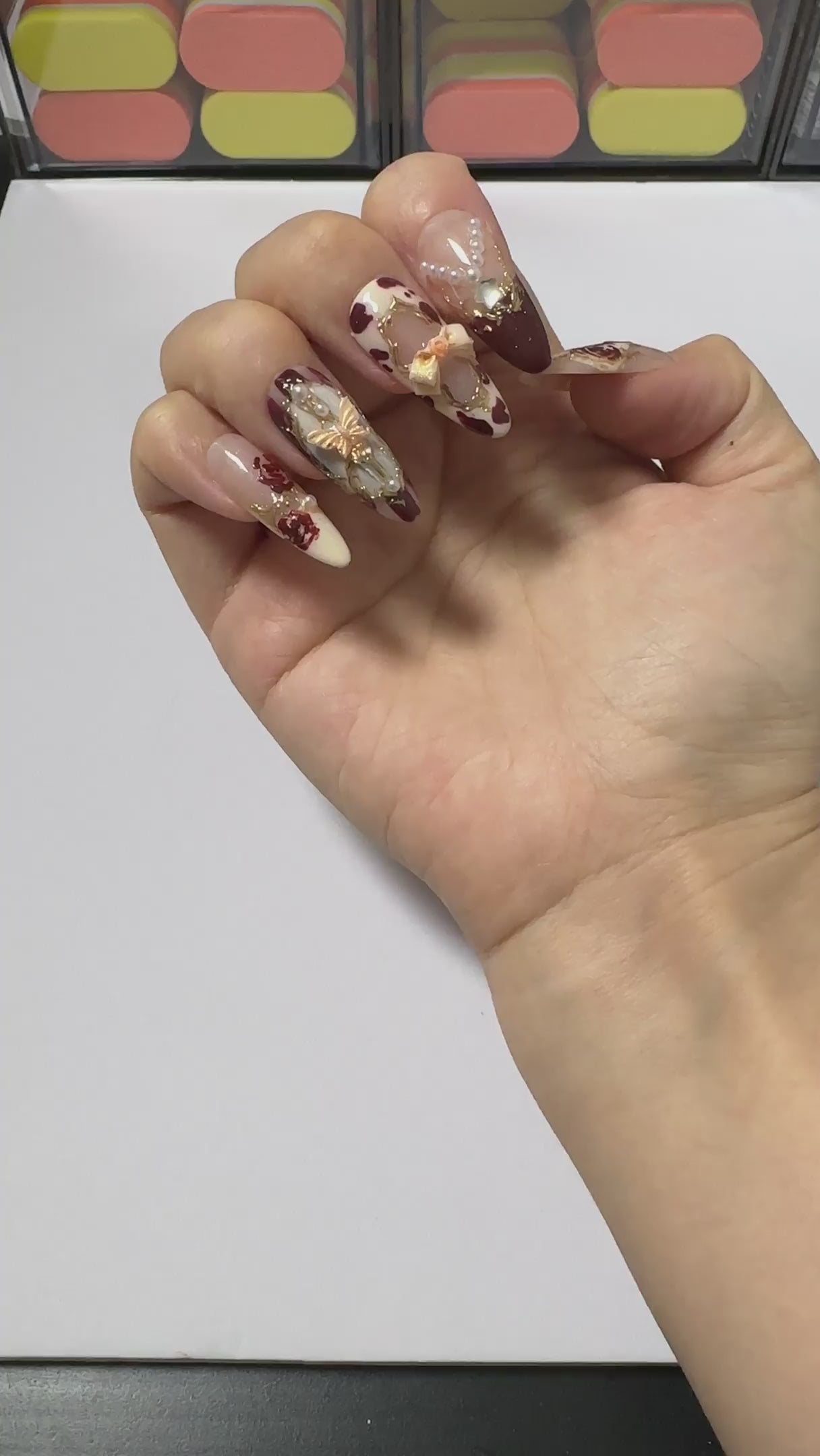Close-up video showcasing 3D gold bows and pearl chains on burgundy coquette handcrafted gel press-on nails Wine Rose by Velvetkay.