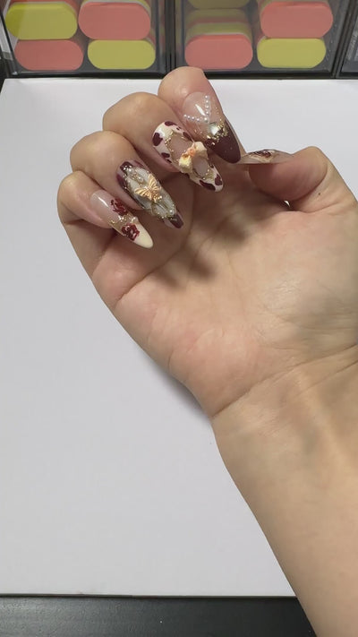 Close-up video showcasing 3D gold bows and pearl chains on burgundy coquette handcrafted gel press-on nails Wine Rose by Velvetkay.