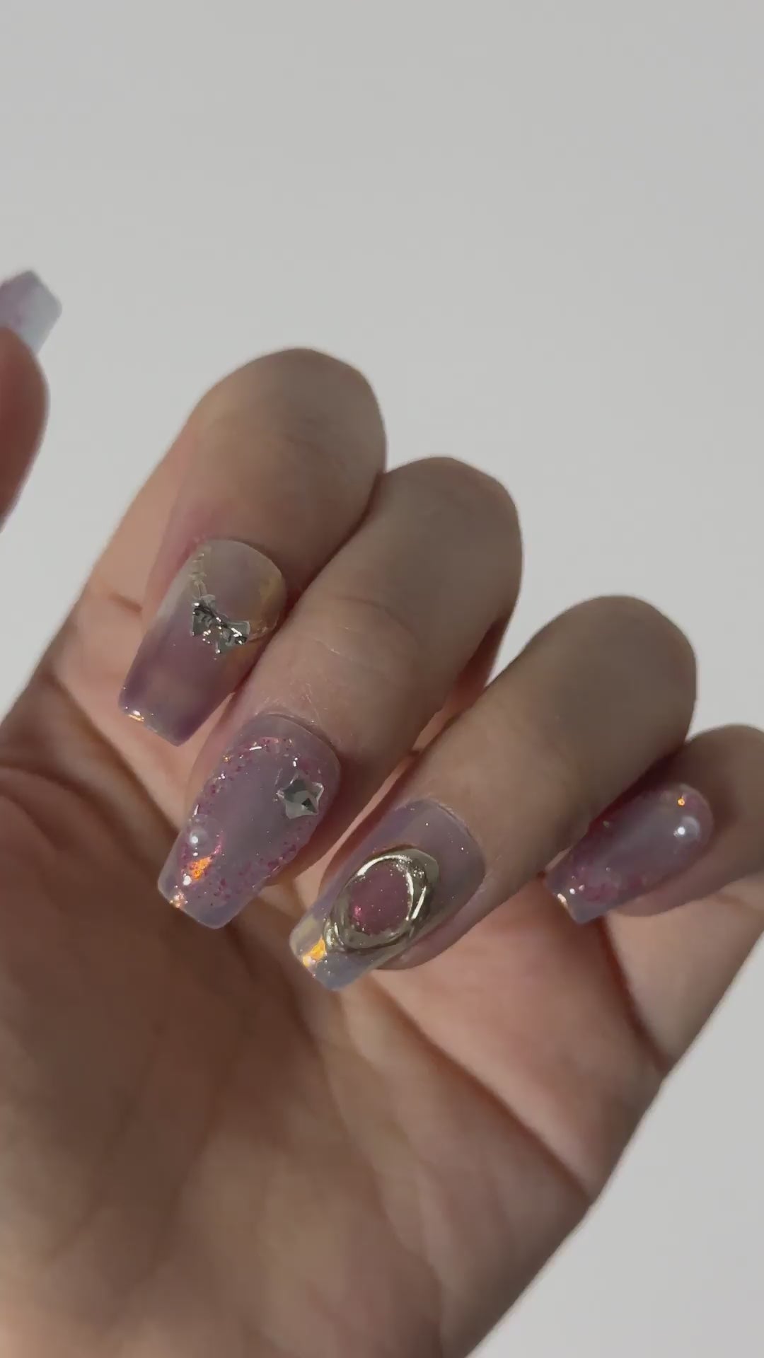 Video showcasing long coffin press on nails with a dreamy purple aura and glitter effect. The design features handcrafted 3D details including a silver planet charm, butterflies, and pearls, creating a mystical fairycore aesthetic.