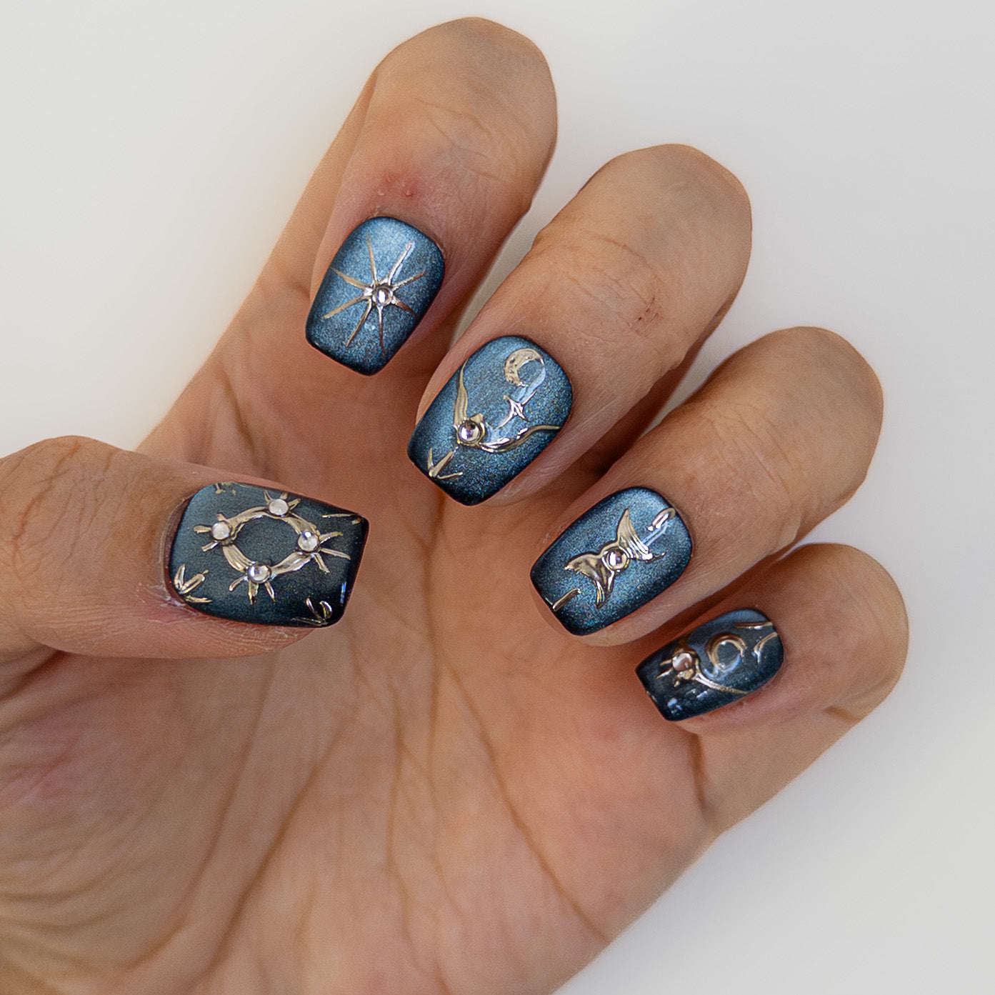 Top down view of Astral Vault press on nails showing thumb detail. 3D silver chrome orbital ring design with gems on a dark blue magnetic base. Designer nail art.