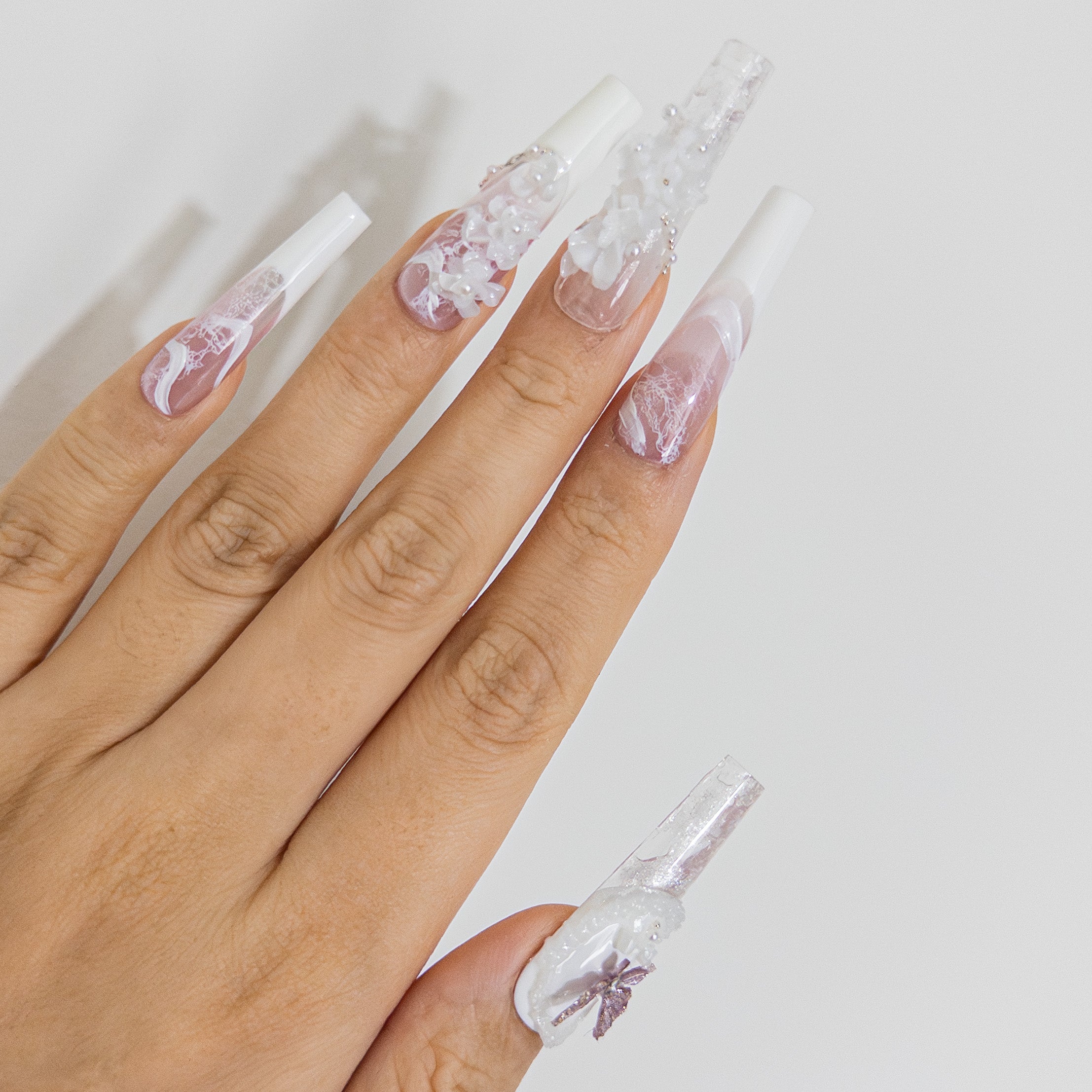 Overhead view of luxury bridal press-on nails displaying a purple butterfly charm, 3D white florals, and elegant lace French tips.